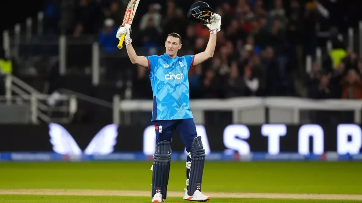 Harry Brook biography: Full-length shot of Harry Brook raising bat and helmet in the England blue ODI kit, celebrating his maiden ODI century against Australia