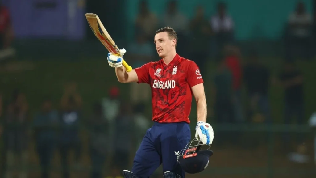 Harry Brook biography: Harry Brook raising his bat in the red England T20 kit after his record century against Pakistan at the T20 World Cup in Pallekele